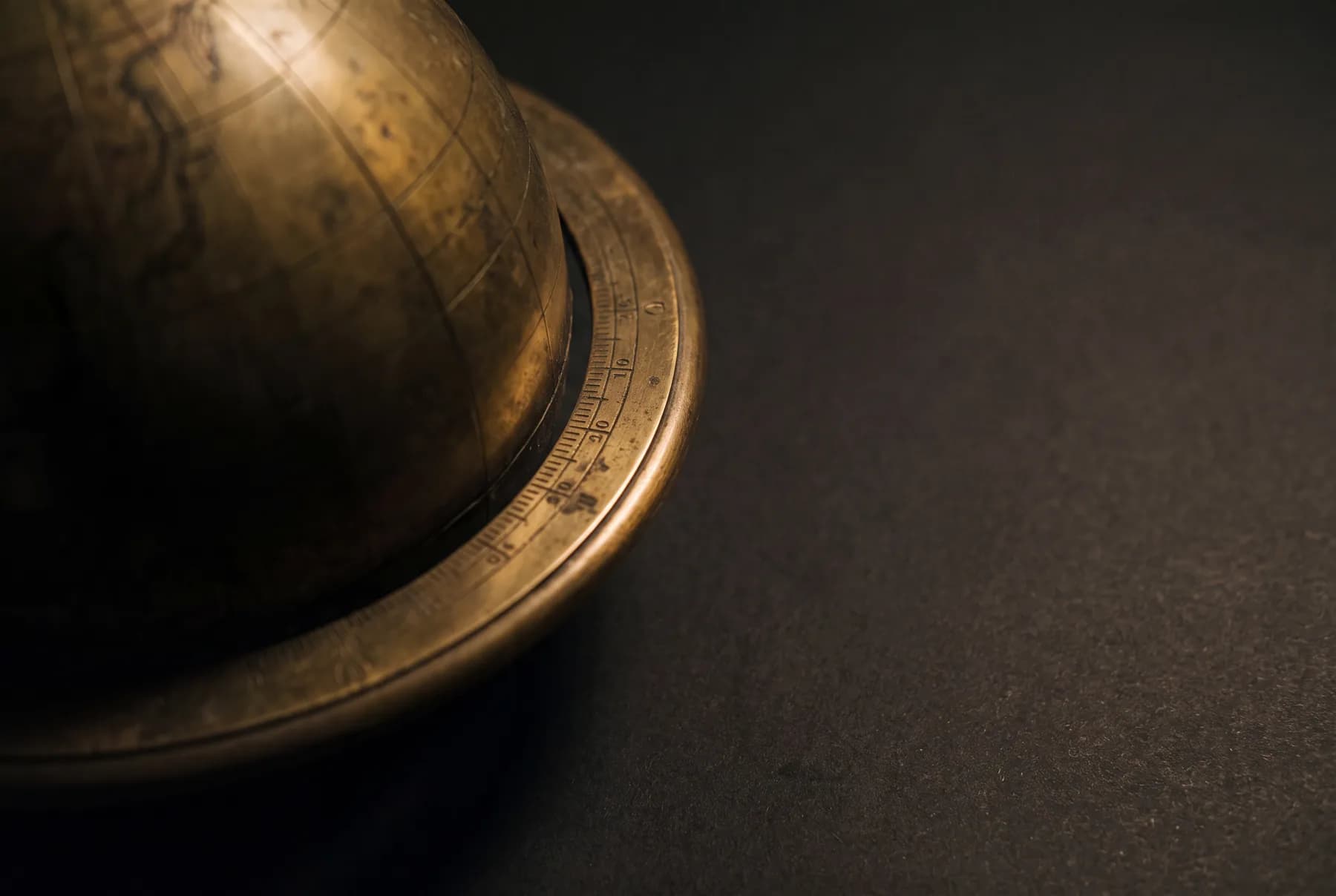 An antique brass globe emerging from shadow — world markets, one sweep